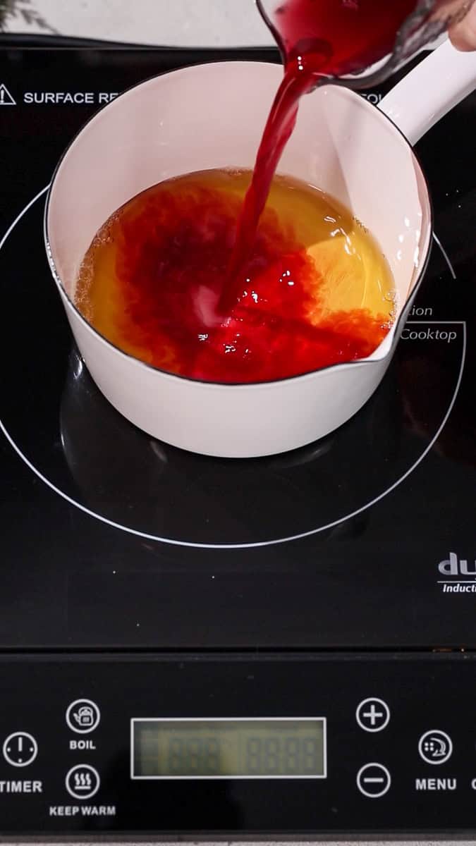 Hand pouring cranberry juice into a saucepan.