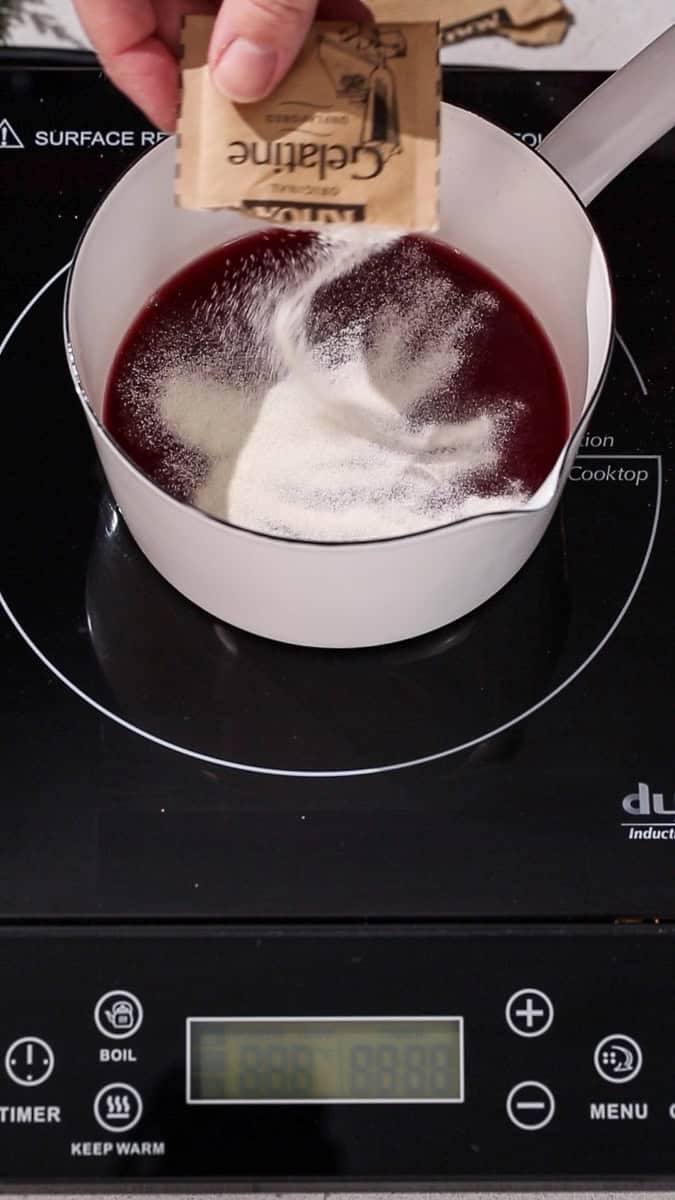 Hand sprinkling powdered gelatin onto the top of red liquid.