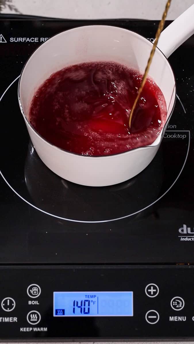 Spoon stirring red liquid in a saucepan over low heat.