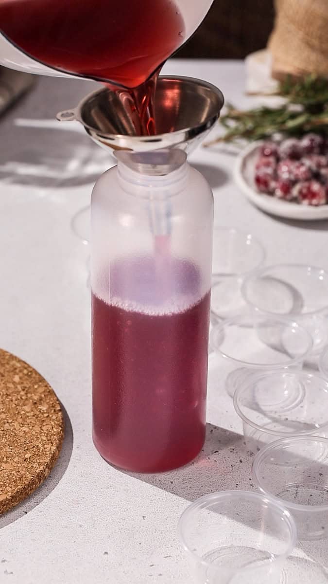 Red liquid being put into a plastic squeeze bottle using a funnel.