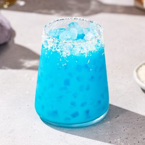 Bright blue colored Jack Frost cocktail with dried coconut on the rim and nugget ice.