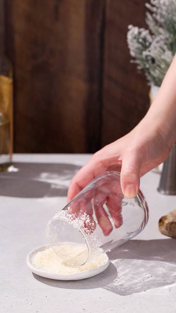 Hand dipping the rim of a cocktail glass into a dish of dried shredded coconut.