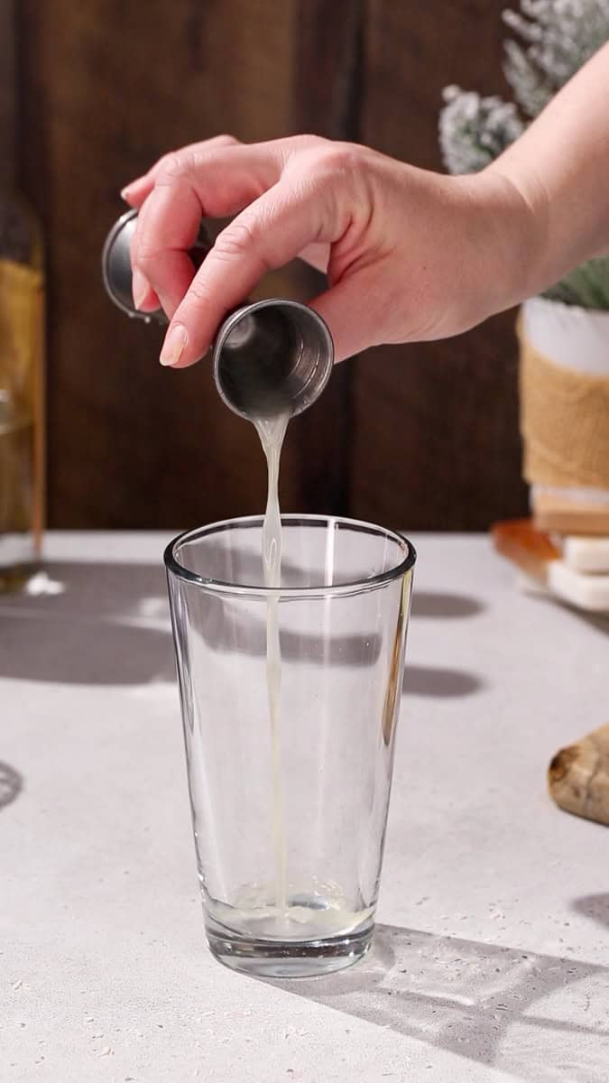 Hand adding lime juice to a cocktail shaker.