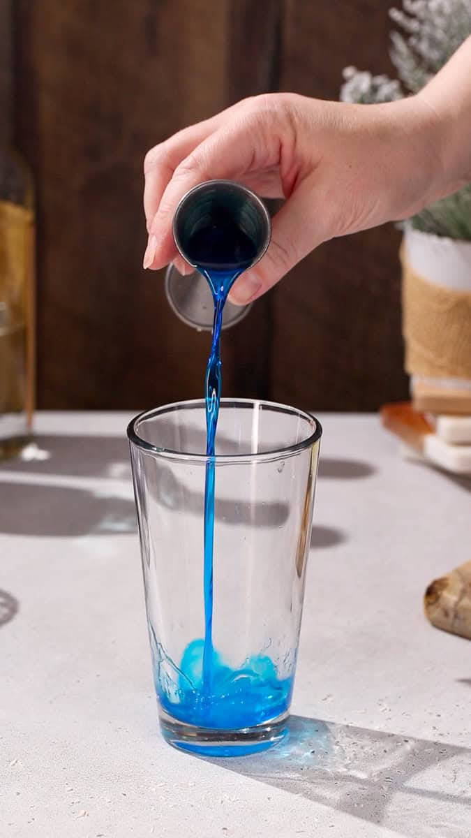 Hand adding Blue Curacao liqueur to a cocktail shaker.