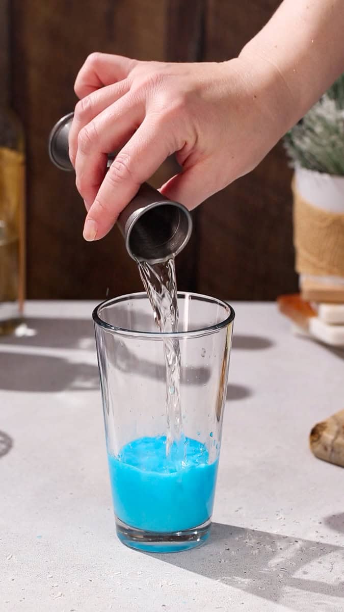 Hand adding white cranberry juice to a cocktail shaker.