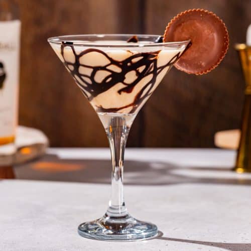 Side view of a Peanut Butter Cup Martini cocktail. The glass has a chocolate drizzle and there is a peanut butter cup candy garnish.