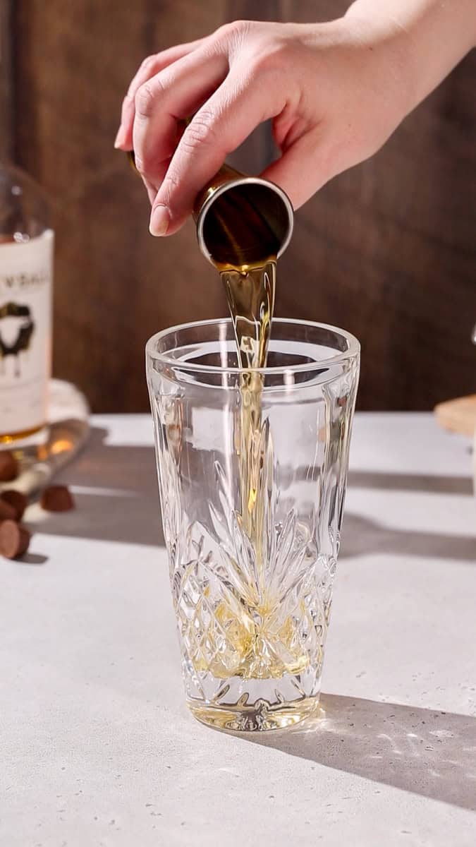 Hand pouring peanut butter whiskey into a cocktail shaker.