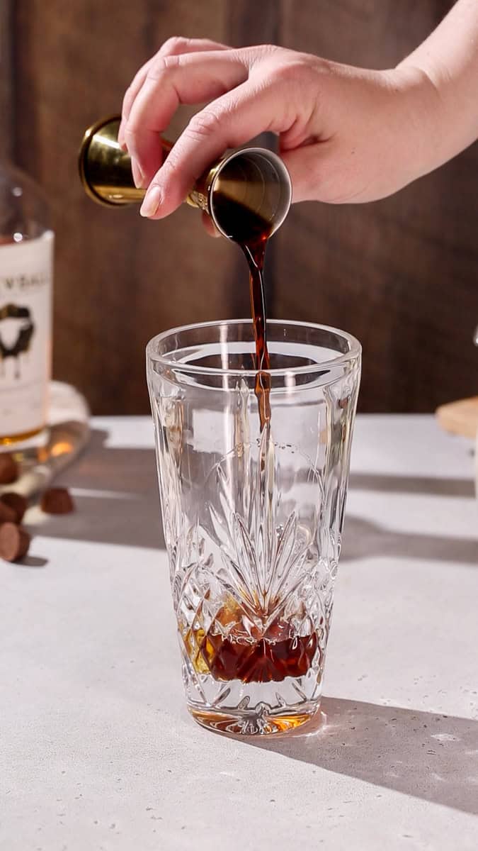 Hand pouring creme de cacao into a cocktail shaker.