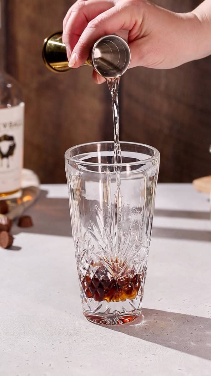 Hand pouring chocolate vodka into a cocktail shaker.