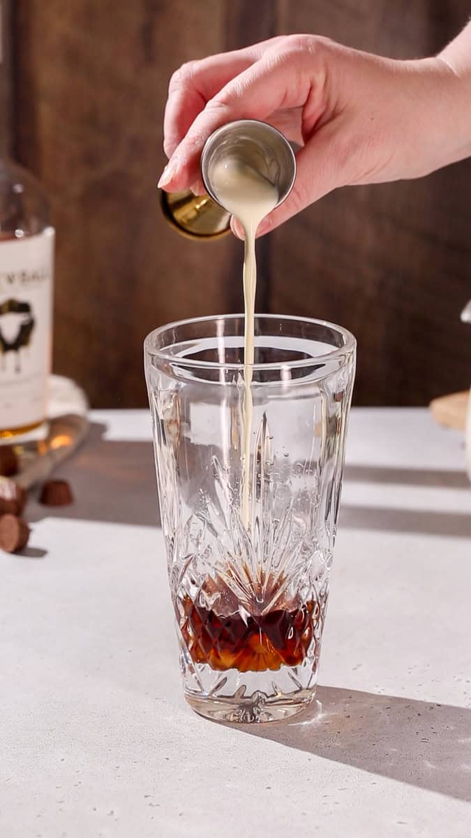 Hand pouring cream into a cocktail shaker.