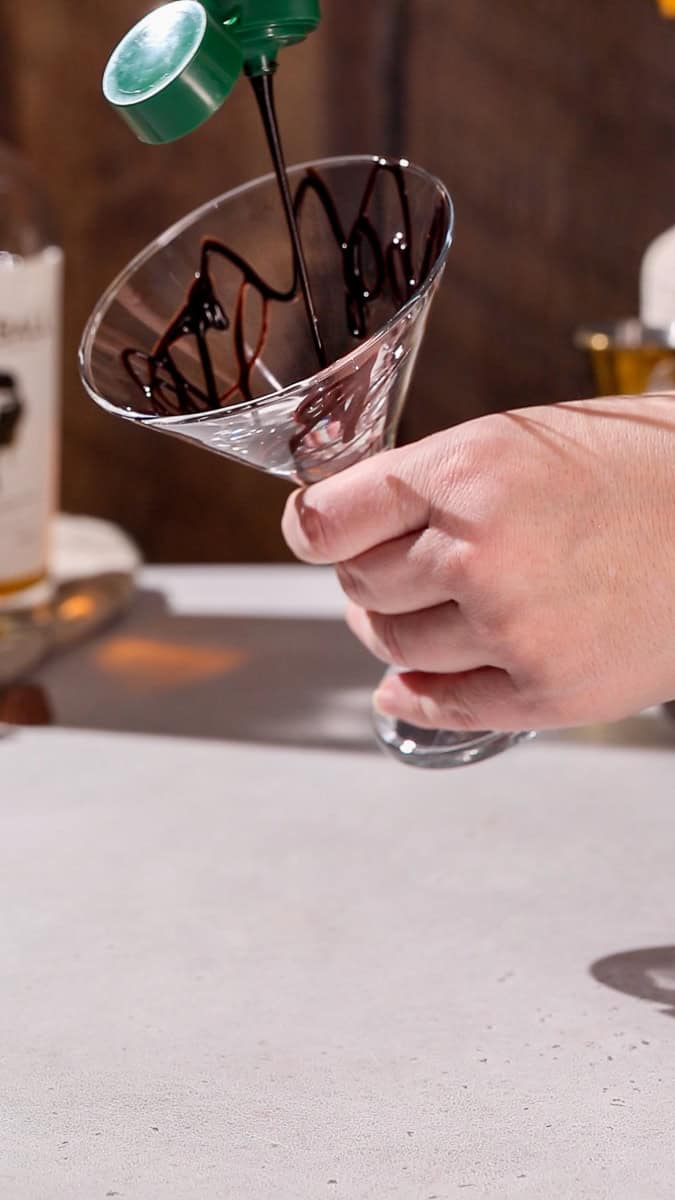 Hand adding a chocolate drizzle to a martini glass.