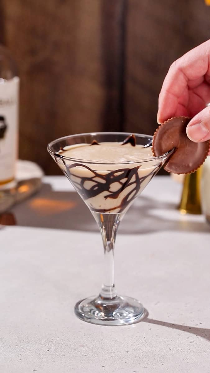 Hand adding a peanut butter cup to the rim of a cocktail glass.