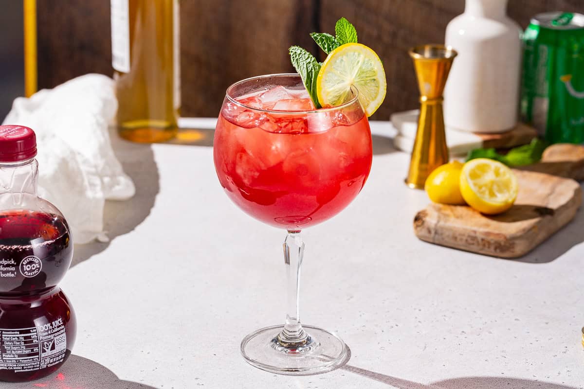 Pomegranate Spritzer Mocktail on a countertop with tools and ingredients in the background.