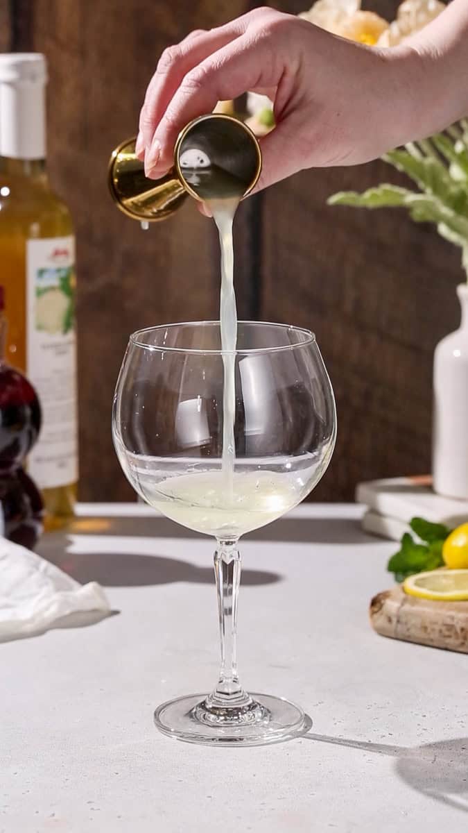 Hand pouring lemon juice into a cocktail glass.