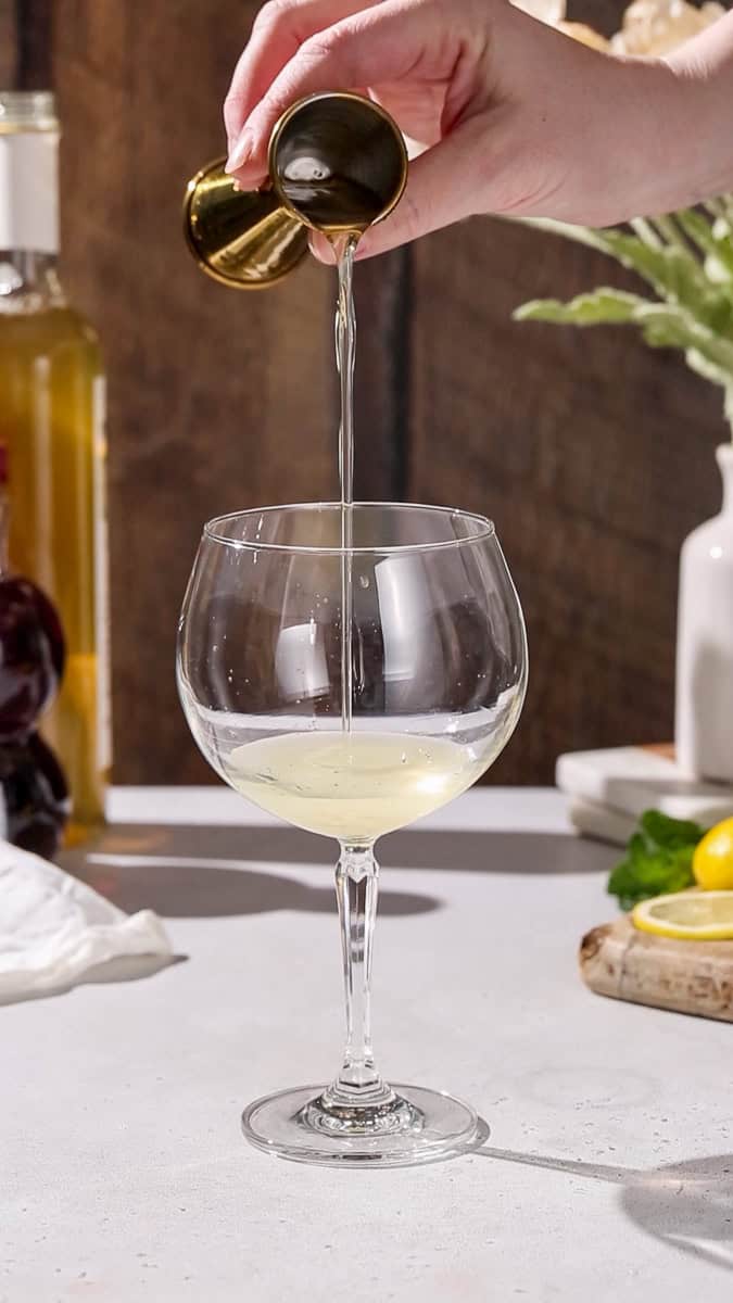 Hand pouring elderflower syrup into a glass.