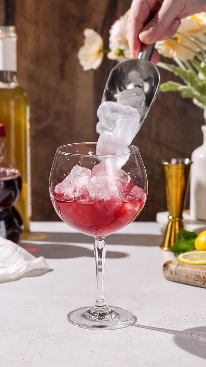 Hand adding ice to a large wine glass.