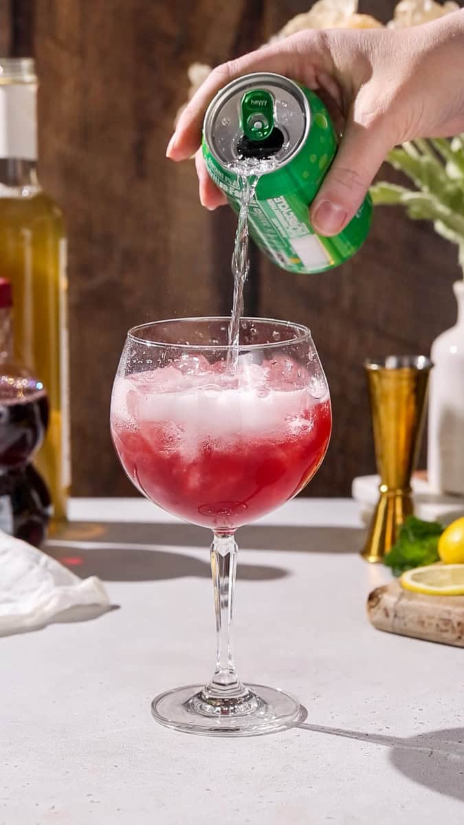 Hand pouring lime seltzer into a large wine glass.