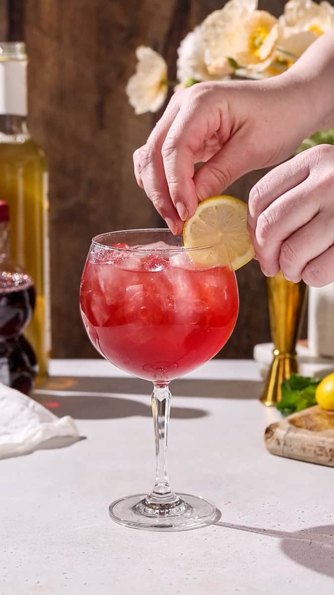 Hand adding a lemon slice garnish to a spritz glass.