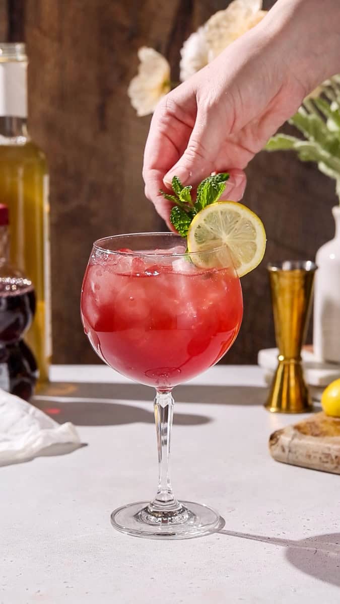 Hand adding a mint sprig to a spritz glass.