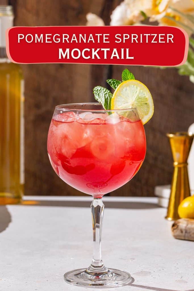 Red colored pomegranate mocktail in a large wine glass. Text above the image says “Pomegranate Spritzer Mocktail”.