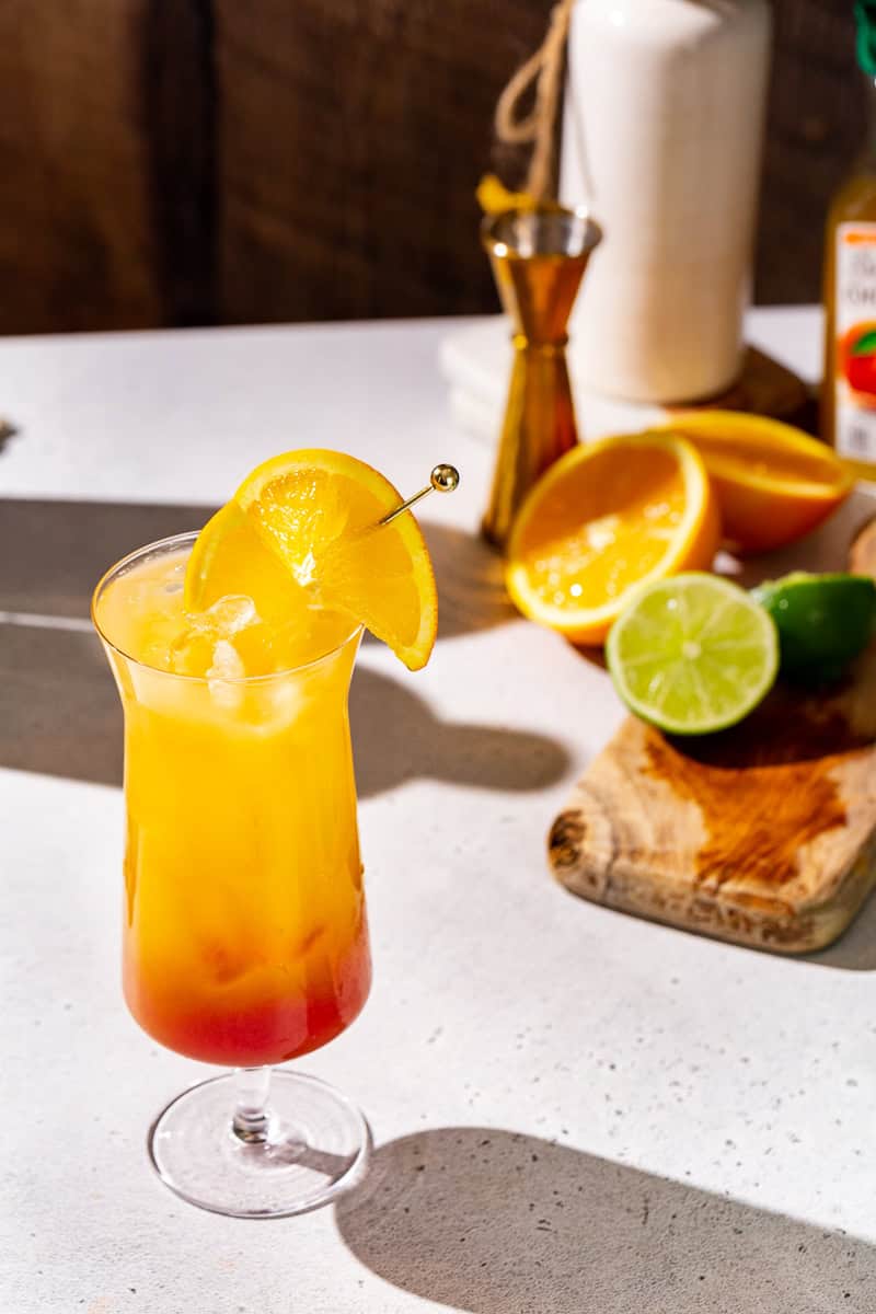 Overhead view of a Tequila Sunrise Mocktail with fruit and a jigger in the background.