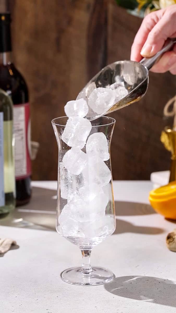 Hand adding ice to a cocktail glass.