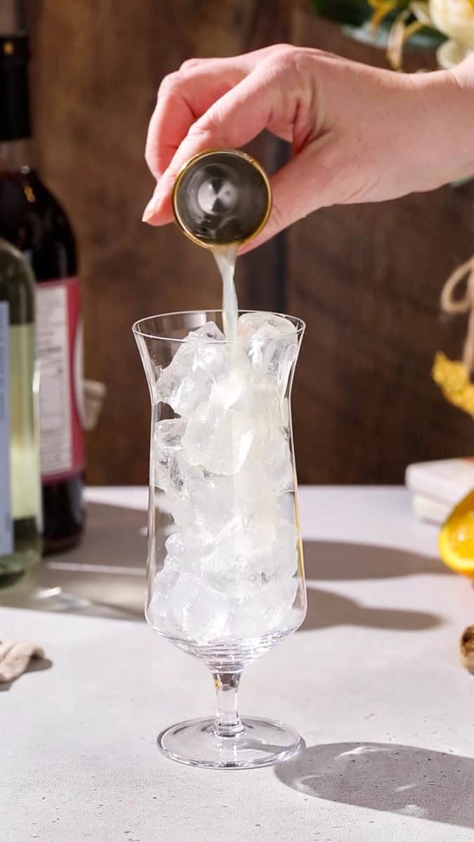 Hand adding lime juice to a cocktail glass.