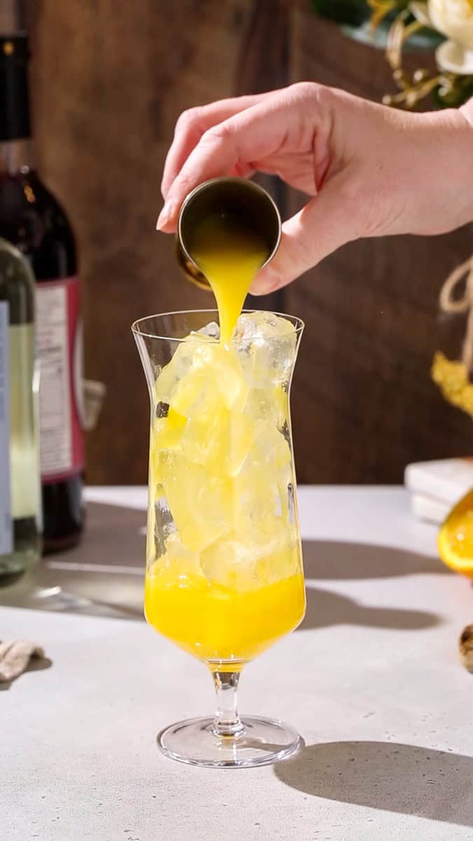 Hand adding orange juice to a cocktail glass.