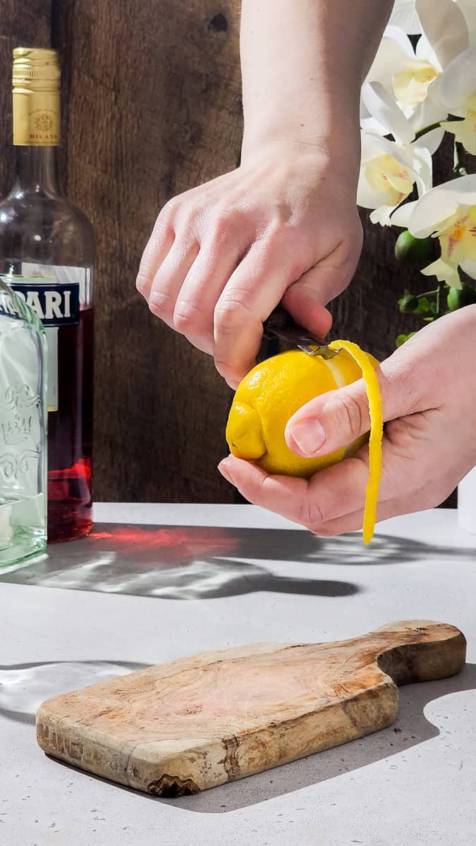 Hand using a channel knife to peel a long strip of lemon peel.