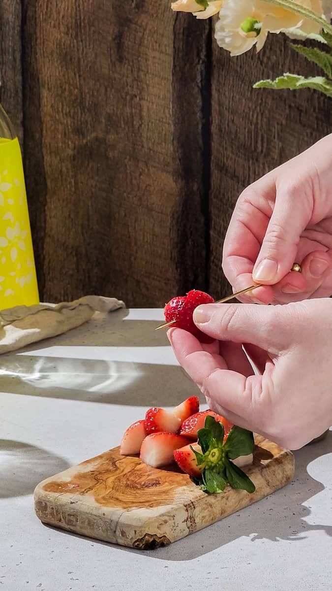 Hand adding a cocktail pick through a heart-shaped strawberry piece.