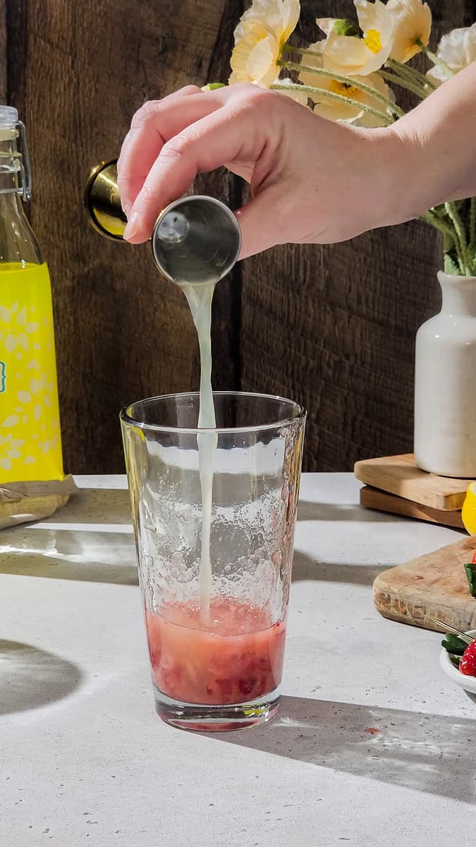 Hand adding lemon juice to a cocktail shaker.