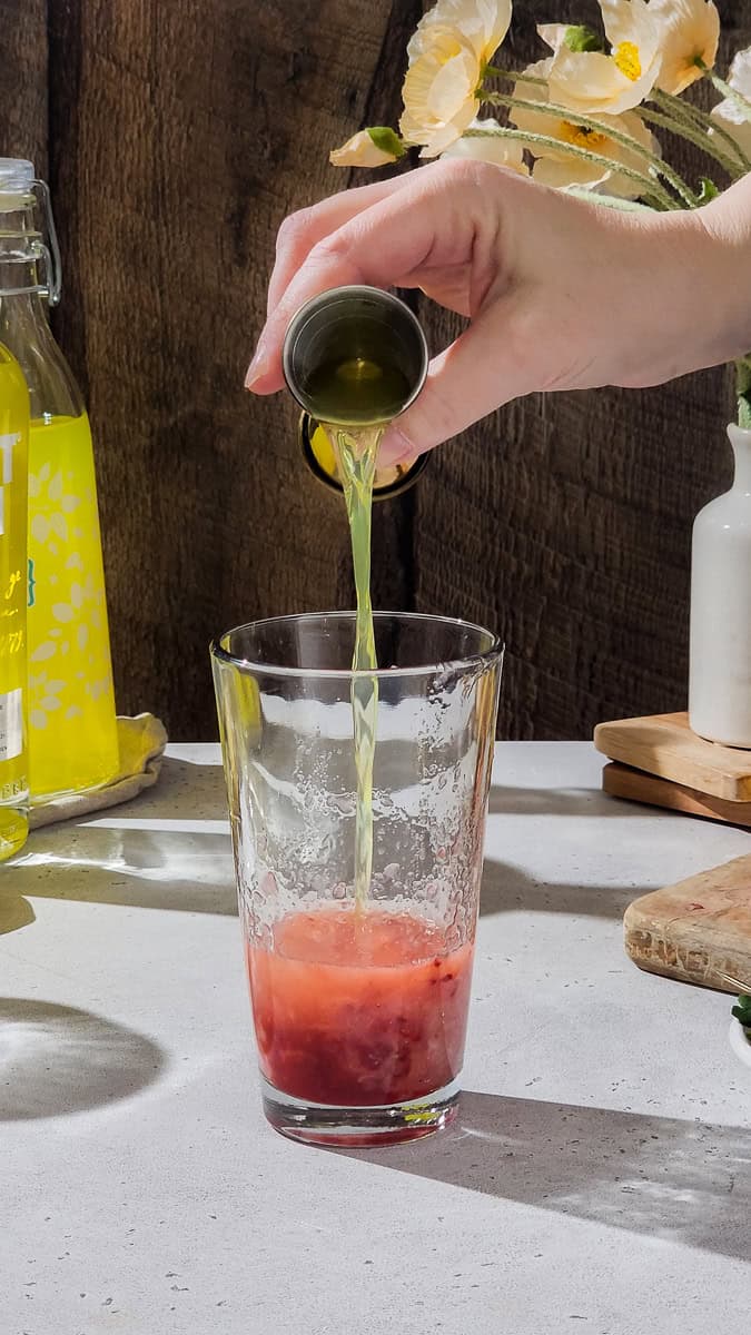 Hand adding limoncello liqueur to a cocktail shaker.