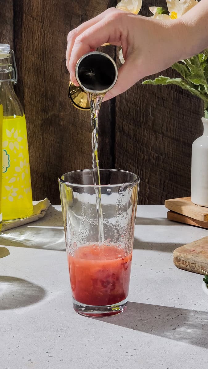 Hand adding citrus vodka to a cocktail shaker.